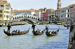 Gondeln auf dem Fluss vor Venedig mit Rialtobrücke im Hintergrund und den bunten Häuserfronten rechts und links