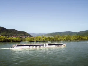 Aufnahme eines AROSA-Flusskreuzfahrtschiffes auf einem Fluss, im Hintergrund leicht hügelige Landschaft mit Wäldern