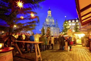 Dresdener Weihnachtsmarkt mit Leuchtsternen, Frauenkirche im Hintergrund, Menschen an den Weihnachtsmarktbuden am Abend