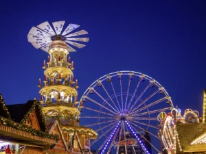 Weihnachtsmarktatmosphäre mit großer Weihnachtspyramide und Riesenrad am Abend