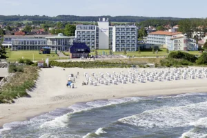 Frontansicht vom Hotel Morada direkt am Strand gelegen, im Vordergrund Strandkörbe in reih und Gleid aufgestellt im Hintergrund Grün und Wald